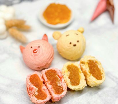 Close-up of cute pink pig and yellow bear swirl pastries with two halved flaky pineapple-jam-filled tarts on a marble surface — colorful Taiwanese-style pineapple pastries from a bakery.