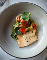 Gourmet plated smoked salmon fillet with baby carrots, salmon roe, edible nasturtium leaves and herb vinaigrette in a white bowl — colorful fine‑dining seafood dish