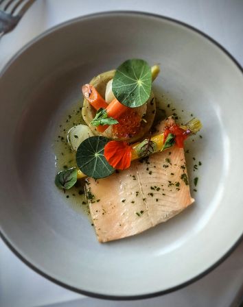 Gourmet plated smoked salmon fillet with baby carrots, salmon roe, edible nasturtium leaves and herb vinaigrette in a white bowl — colorful fine‑dining seafood dish