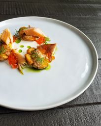 Gourmet plated appetizer on a large white plate: smoked salmon and seared baby potatoes topped with orange salmon roe, dill sprigs and drops of green herb oil on a dark wooden table.