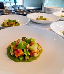 Gourmet plated starter: diced salmon and avocado on a bright green pea purée, garnished with croutons and micro herbs, staged on white plates in a restaurant kitchen.