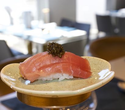 Bright pink tuna nigiri crowned with black caviar on a speckled ceramic plate in a modern sushi restaurant setting