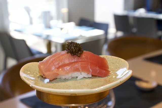 Bright pink tuna nigiri crowned with black caviar on a speckled ceramic plate in a modern sushi restaurant setting