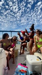 Group of friends in colorful bikinis laughing and popping champagne on a sunny boat party under a sweeping bay bridge and dotted blue sky