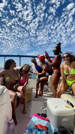 Group of friends in colorful bikinis laughing and popping champagne on a sunny boat party under a sweeping bay bridge and dotted blue sky