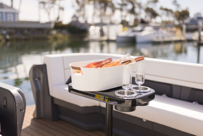 Rosé wine bottles chilling in a white ice tub with two champagne flutes on a glossy black table aboard a boat at a sunny marina waterfront