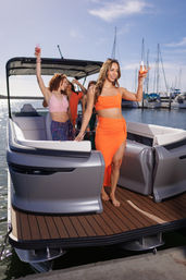 Group of women celebrating with champagne on a pontoon boat at a sunny marina, sailboat masts and docks in the background.