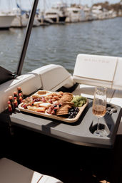Charcuterie board with crackers, cheeses, grapes, blueberries, cured meats and nuts on a boat table beside a glass of rosé, soft-focus marina and docked yachts in the background.