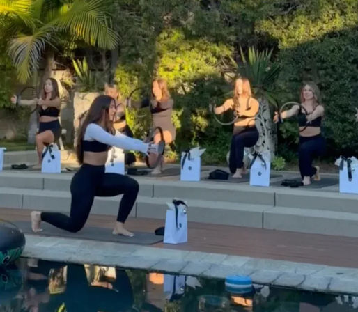Sunlit outdoor poolside Pilates group: women on mats doing lunges and using Pilates rings beside a backyard pool