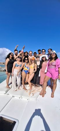 Large group of friends enjoying a yacht party in swimwear on a sunny day, clear blue sky and turquoise tropical coastline in the background