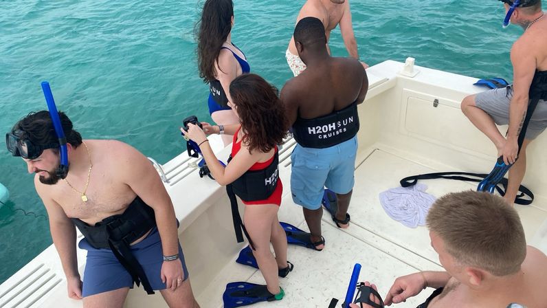 Group of snorkelers on a white boat deck preparing to enter turquoise water, putting on blue snorkel masks, fins and life vests.