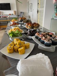 Home buffet spread on a dining table in a modern apartment — grilled corn on the cob, mini burgers, fries, salad, tortilla chips and decorated cupcakes for a party.