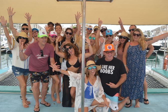 Energetic group of adults cheering on a sunny boat deck at a marina — summer boat party with hats, sunglasses, swimsuits and colorful caps