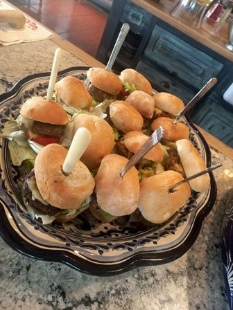 Cheeseburger sliders with lettuce and cheese on a decorative ceramic platter, skewered and served on a granite kitchen countertop - party appetizer platter