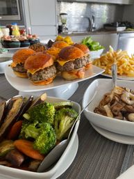 Cheeseburger sliders on glossy brioche buns on a platter with crispy fries, roasted broccoli and mixed vegetables, and sautéed mushrooms on a home kitchen buffet.