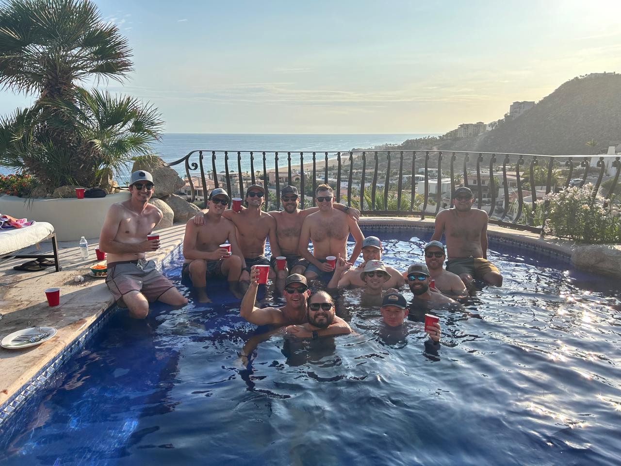 Group of friends enjoying a pool party with red cups in a terrace plunge pool overlooking the ocean and hillside at sunset, coastal vacation vibe