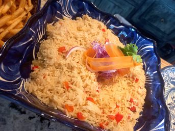 Seasoned long-grain rice with diced red bell pepper, topped with carrot ribbons, shredded purple cabbage and cilantro, served in a decorative blue ceramic bowl with a side of fries