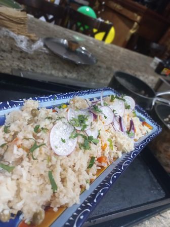 Colorful vegetable rice salad topped with thin radish slices, red onion and cilantro on a decorative blue rectangular serving platter, close-up on a kitchen countertop.