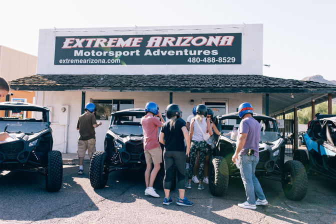 Helmeted adults gathering around off-road UTVs outside a motorsport adventure office in Arizona, preparing for a desert tour.