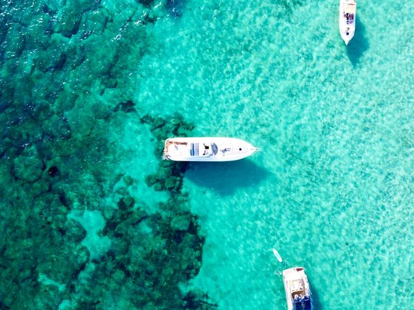 Aerial drone view of white motorboats anchored over crystal-clear turquoise water showing coral reef patterns and sandy seabed