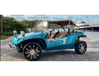 Sleek turquoise open-top dune buggy with tan seats and chrome headlights parked at a coastal marina beside yachts and a wooden dock