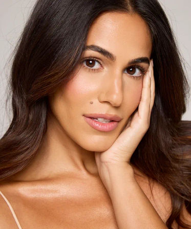 Close-up studio beauty headshot of a smiling woman with long dark hair, glowing skin, natural makeup and hand on her cheek — skincare and cosmetics portrait