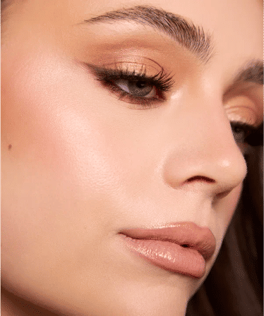 Glam beauty close-up: shimmery gold eyeshadow, soft winged eyeliner, long lashes, glossy nude lips and dewy highlighted skin.