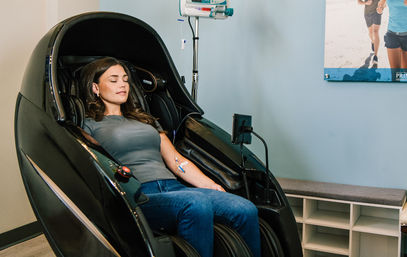 Woman relaxing in a futuristic black recovery pod receiving IV hydration therapy at a wellness clinic, arm IV line connected to an infusion pump.
