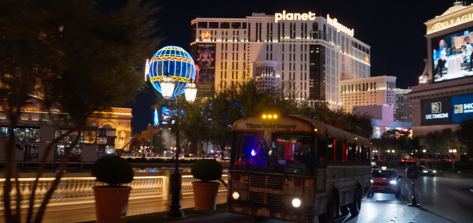 Las Vegas Strip at night with a neon-lit globe sign, retro party bus at the curb, palm trees and illuminated hotel towers