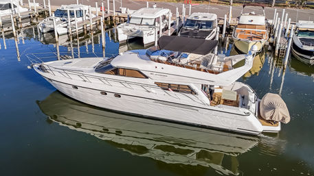 Sleek white motor yacht lounging at a sunny marina with a covered flybridge and a dinghy at the stern, crisp reflections rippling in calm water