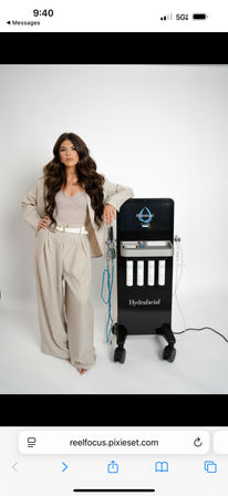 Person in a beige pinstripe suit posing with a professional skincare facial machine on wheels in a white studio — touchscreen device with four product cartridges, ideal for spa and medspa treatments.