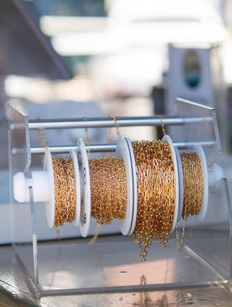 Spools of gold-tone jewelry chain on a clear acrylic rack — sparkling chains for jewelry-making and crafts.