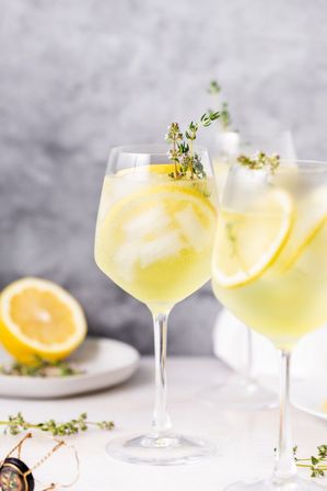 Refreshing lemon-thyme spritz in a wine glass with ice and lemon slices, garnished with fresh thyme and styled on a bright tabletop