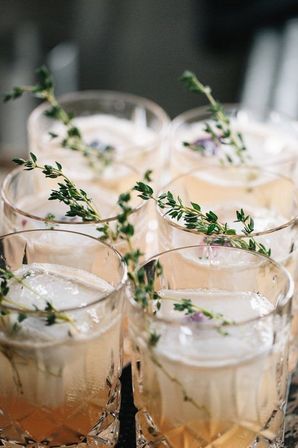 Six crystal lowball cocktails with large square ice cubes and fresh thyme sprigs, pale peach craft drinks styled for a summer brunch or celebration.