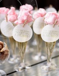 Champagne flutes topped with pink cotton candy and round tags reading 'Pop the bubbly, I'm getting a hubby!' — playful bridal shower garnish