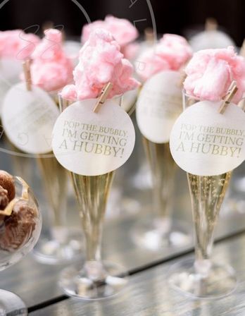 Champagne flutes topped with pink cotton candy and round tags reading 'Pop the bubbly, I'm getting a hubby!' — playful bridal shower garnish