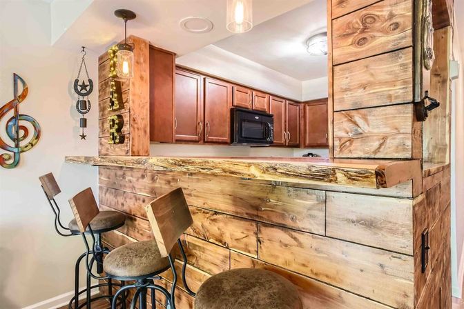 Rustic reclaimed-wood breakfast bar with three metal swivel bar stools, pendant lights, and a kitchen with brown cabinets and microwave