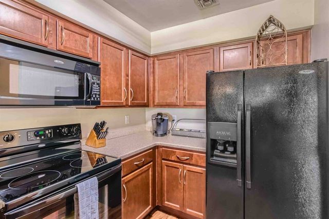 Cozy modern kitchen corner with warm wood cabinets, laminate counters, black smooth-top electric range and microwave, side-by-side fridge with water dispenser, knife block and single-serve coffee maker.
