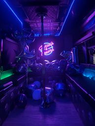Vibrant neon-lit party lounge with a center dance pole, purple-blue LED glow, scattered metallic balloons and a glowing sign that reads "Cocktails & Dreams".