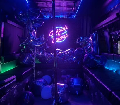 Vibrant neon-lit party lounge with a center dance pole, purple-blue LED glow, scattered metallic balloons and a glowing sign that reads "Cocktails & Dreams".