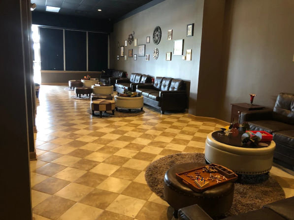 Cozy indoor lounge with dark leather sofas, round ottomans and board games on a checkerboard tile floor beneath gallery-style wall decor.