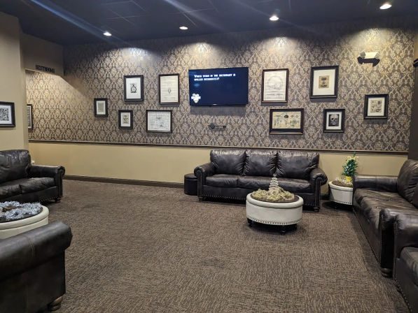 Cozy commercial lounge waiting room with dark leather sofas, patterned wallpaper, framed art, wall-mounted TV, round ottoman and carpeted floor.