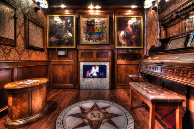 Cozy vintage wood-paneled parlor with a lit fireplace, framed portraits and coat of arms, compass-rose floor medallion, carved antique piano and tufted bench under warm ambient lighting.