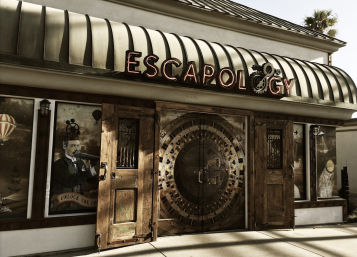 Steampunk-style escape room storefront with curved metal awning, illuminated retro sign, ornate wooden doors flanking a large circular vault door and illustrated window murals.