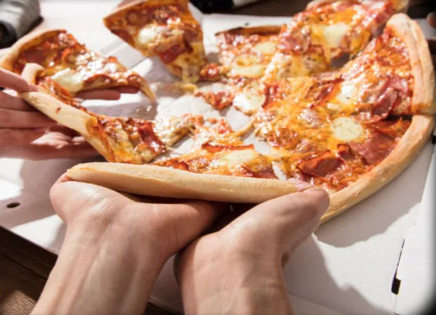 Hands grabbing slices of a hot, melty pepperoni and cheese pizza from an open delivery box on a table