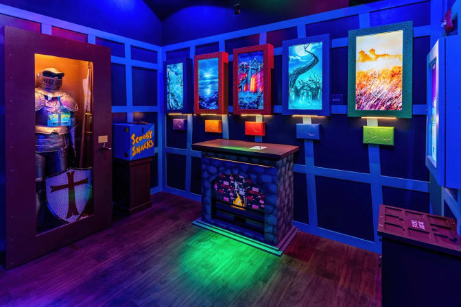 Vibrant neon-lit indoor escape-room set with glassed medieval knight armor, glowing fantasy paintings, faux stone desk and snack chest