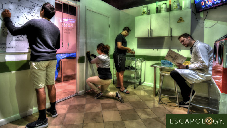 Group of four in a laboratory-themed escape room solving puzzles — person writing chemistry on a whiteboard, one kneeling at a door, another handling props, and a player in a lab coat reading instructions amid cabinets and hazard signs, indoor team puzzle experience.