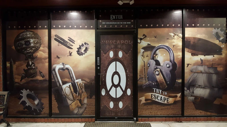 Steampunk-themed escape room storefront mural with oversized antique padlocks and gears, airship and sailing ship artwork, central door labeled "Enter" and a banner reading "Try to Escape".