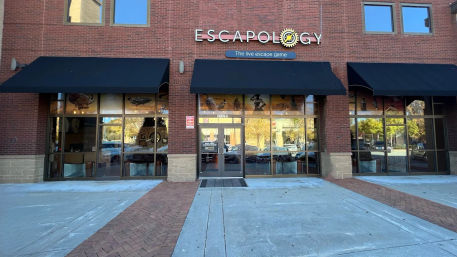 Brick storefront escape room venue with black awnings, large reflective glass windows and double glass doors on a downtown pedestrian plaza.