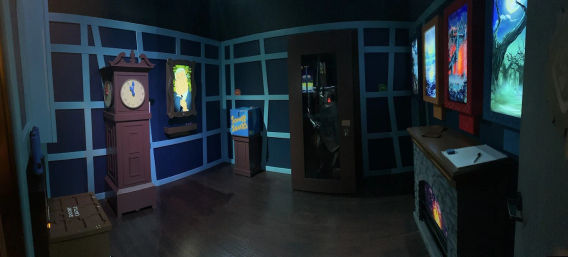 Dimly lit themed puzzle room with blue paneled walls, an antique grandfather clock, illuminated portrait, snack box on a pedestal, dark glass cabinet, and a glowing faux fireplace beneath framed fantasy artwork.